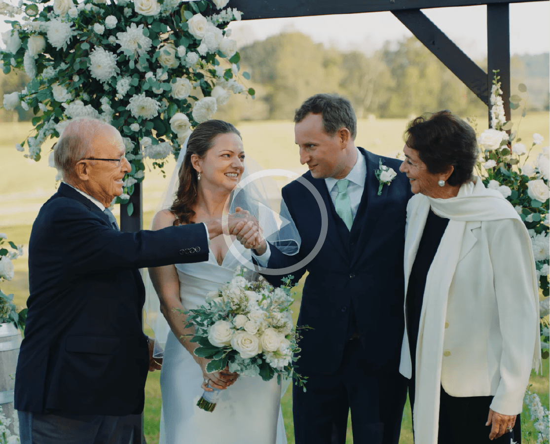 Bride and groom exchanging vows under a white floral arch at an outdoor ceremony