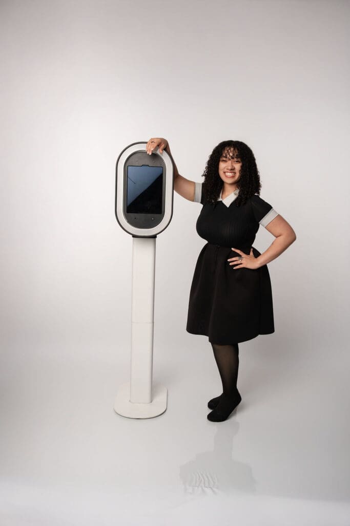 A woman in a black dress poses confidently next to a tall cylindrical white air purifier against a neutral white background.