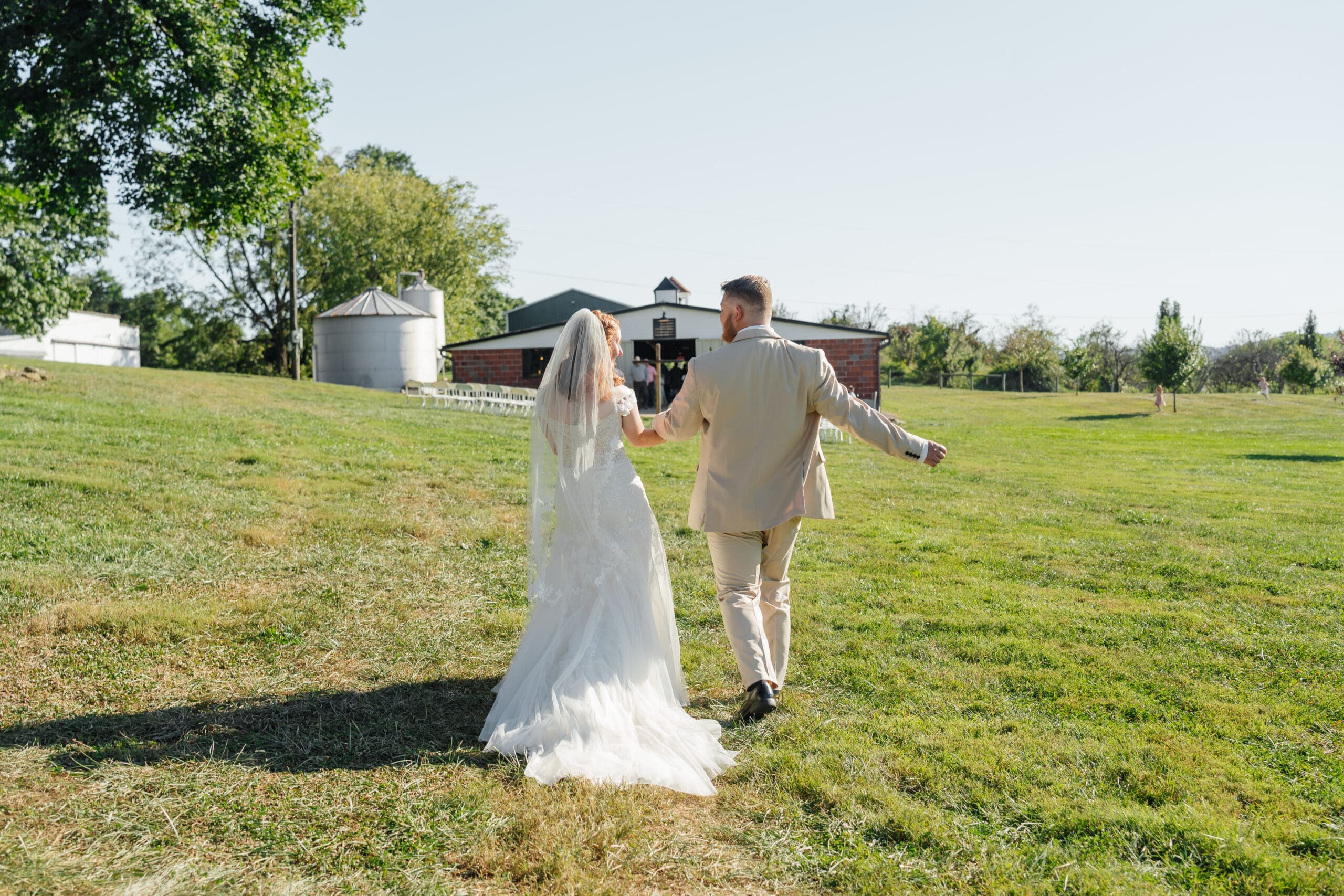 Bride and groom walking hand in hand through an open field