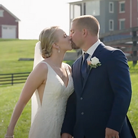 A bride and groom share a tender moment together in a rural farmland setting during golden hour, with a barn and fencing visible in the background.