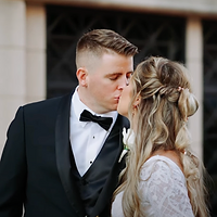 A groom and bride share a tender moment in close-up during their wedding, with soft golden hour lighting and a formal venue backdrop.