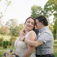 A couple shares an intimate, joyful embrace outdoors in a lush garden setting during daytime.
