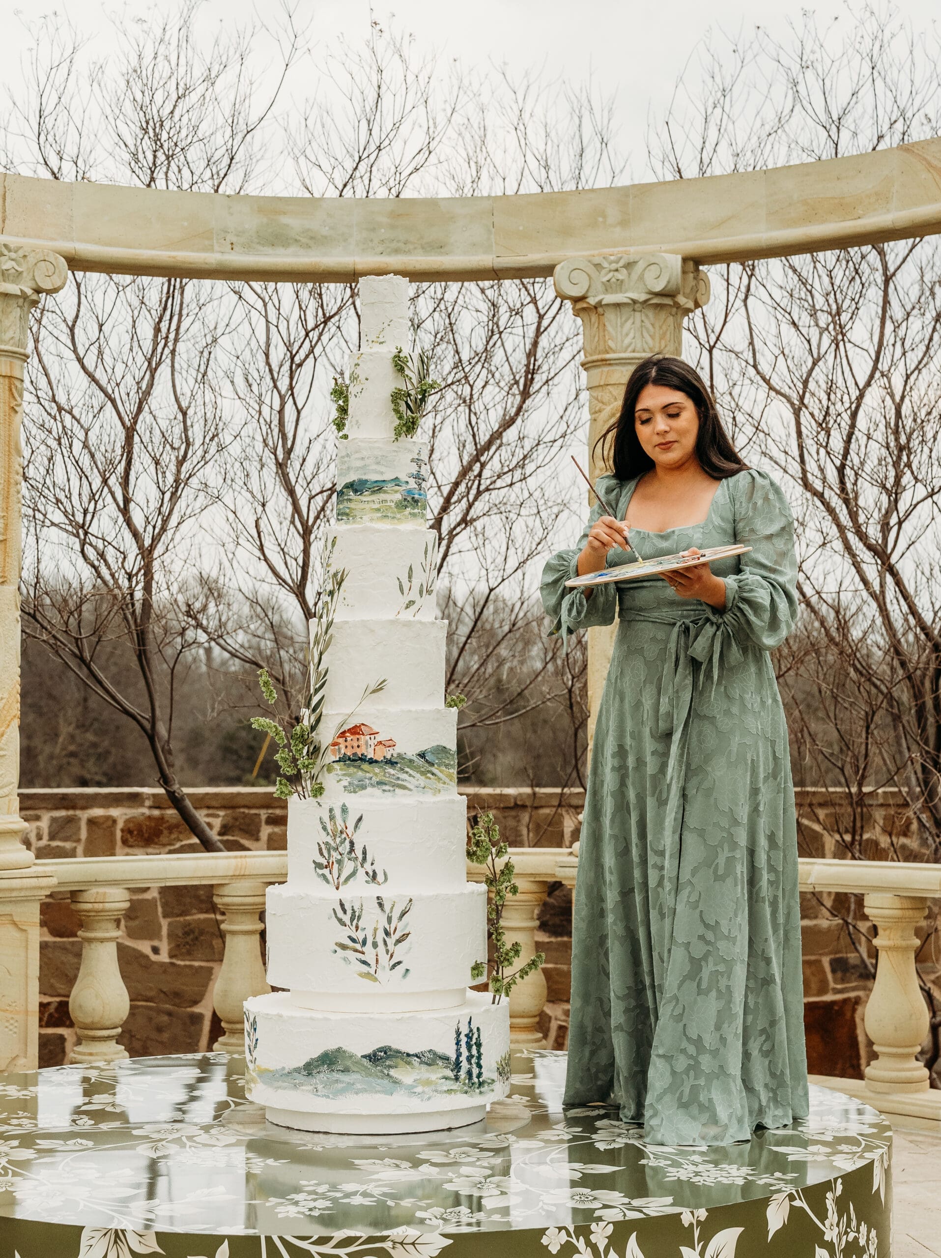 Bride in a sage green dress beside an elegant tiered wedding cake