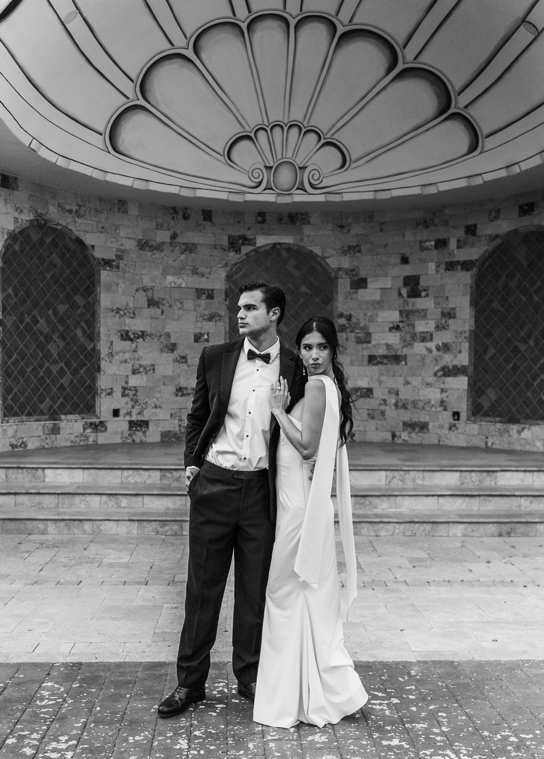 Black and white portrait of a bride and groom at a stone wall