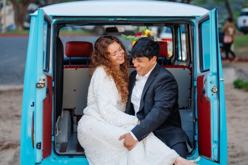 A bride and groom pose together inside a turquoise van with red interior seats during their wedding celebration.