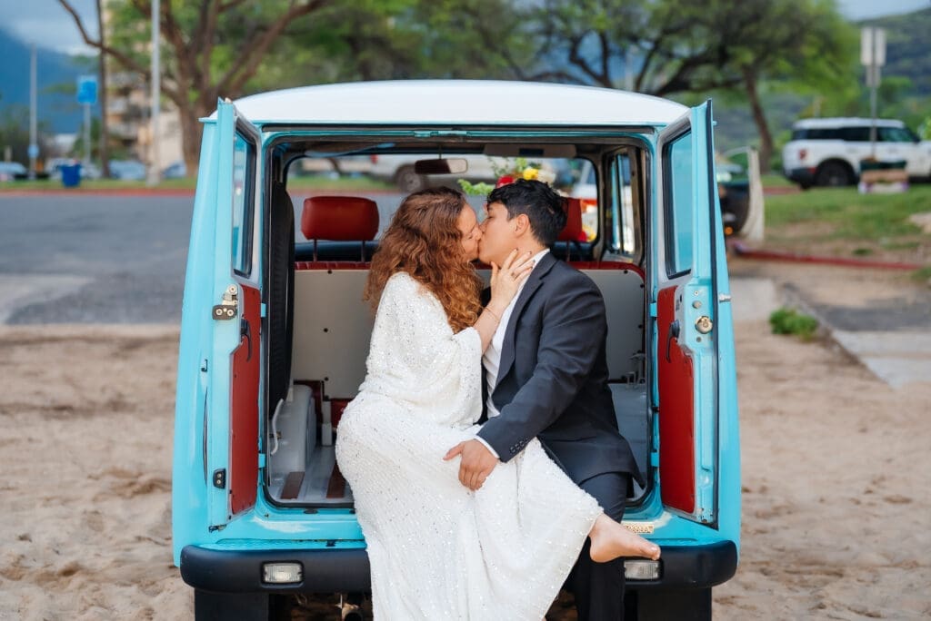 A bride and groom share an intimate moment inside a vintage turquoise van on a beach during their wedding day.
