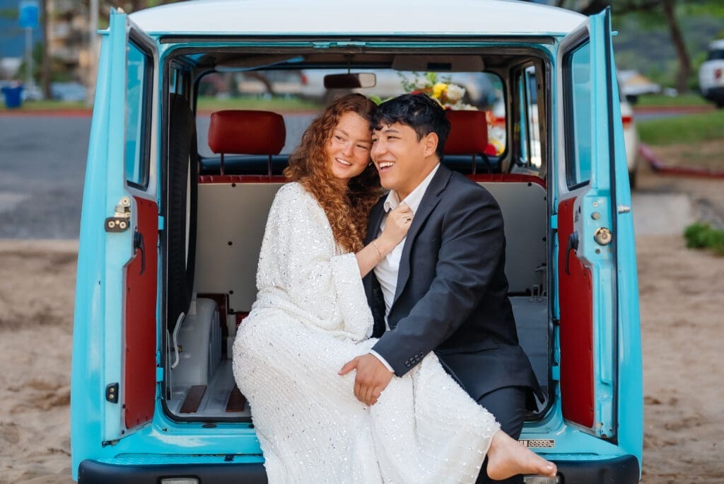 A bride and groom pose together inside the open back of a turquoise and red vintage van on their wedding day.